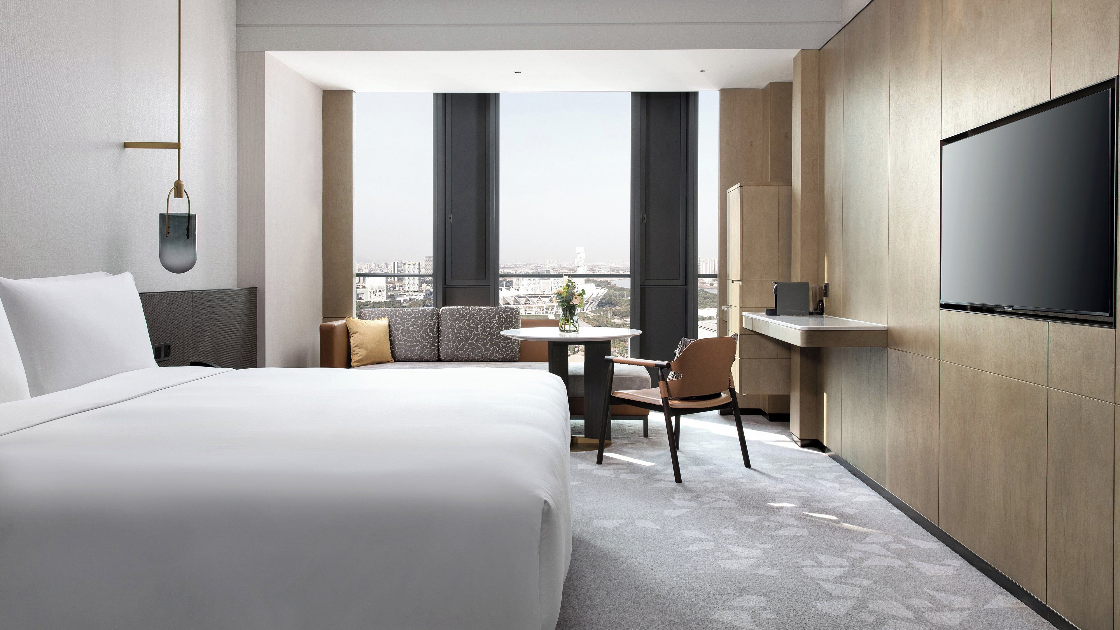 Habitación de hotel con una cama grande, una mesita pequeña, una silla, un televisor y vistas a la ciudad.