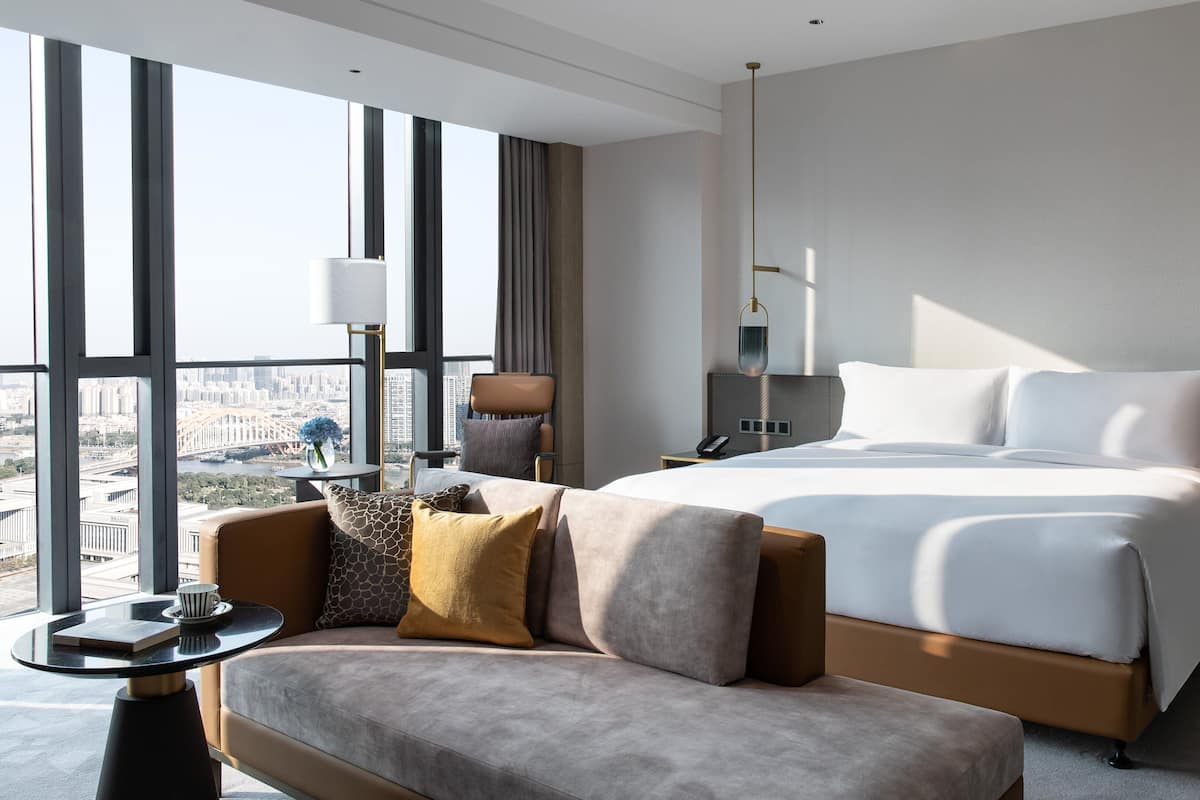A modern hotel room with a large bed, a sofa, a small table, and a nightstand.