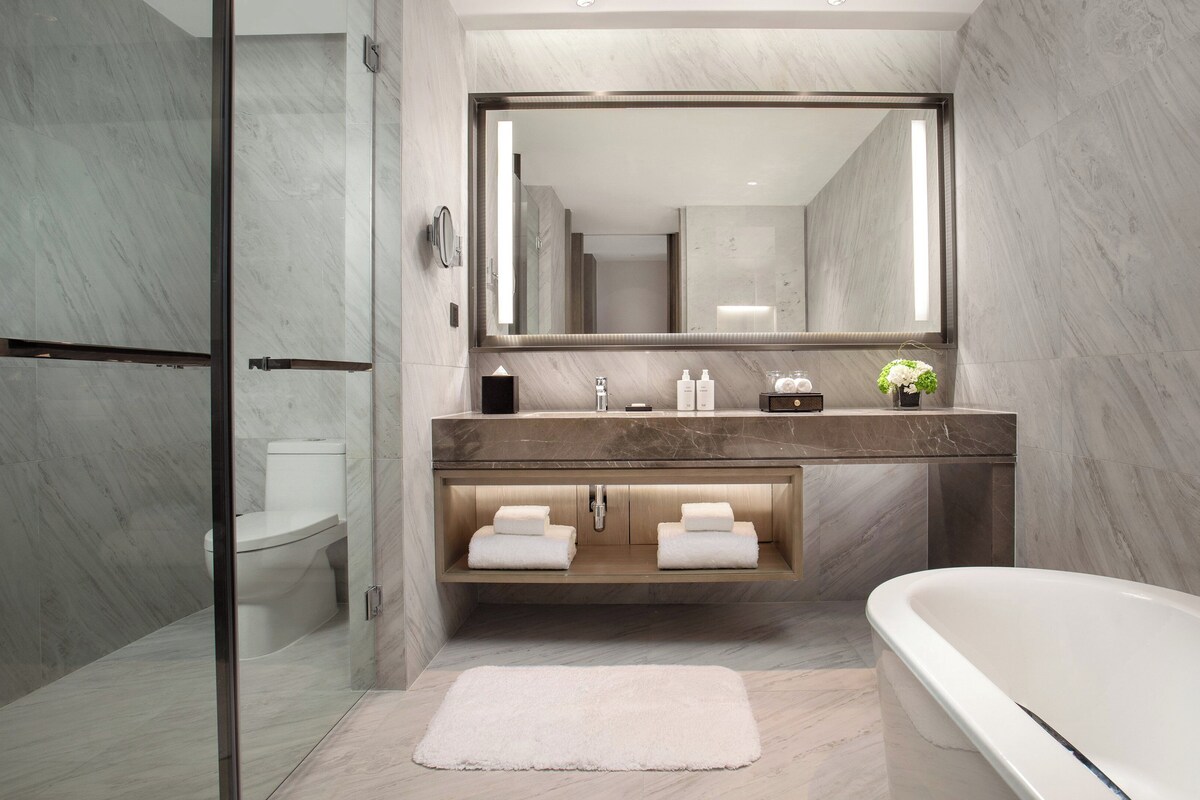 A modern bathroom with a marble vanity, a large mirror, a bathtub, and a glass shower enclosure.