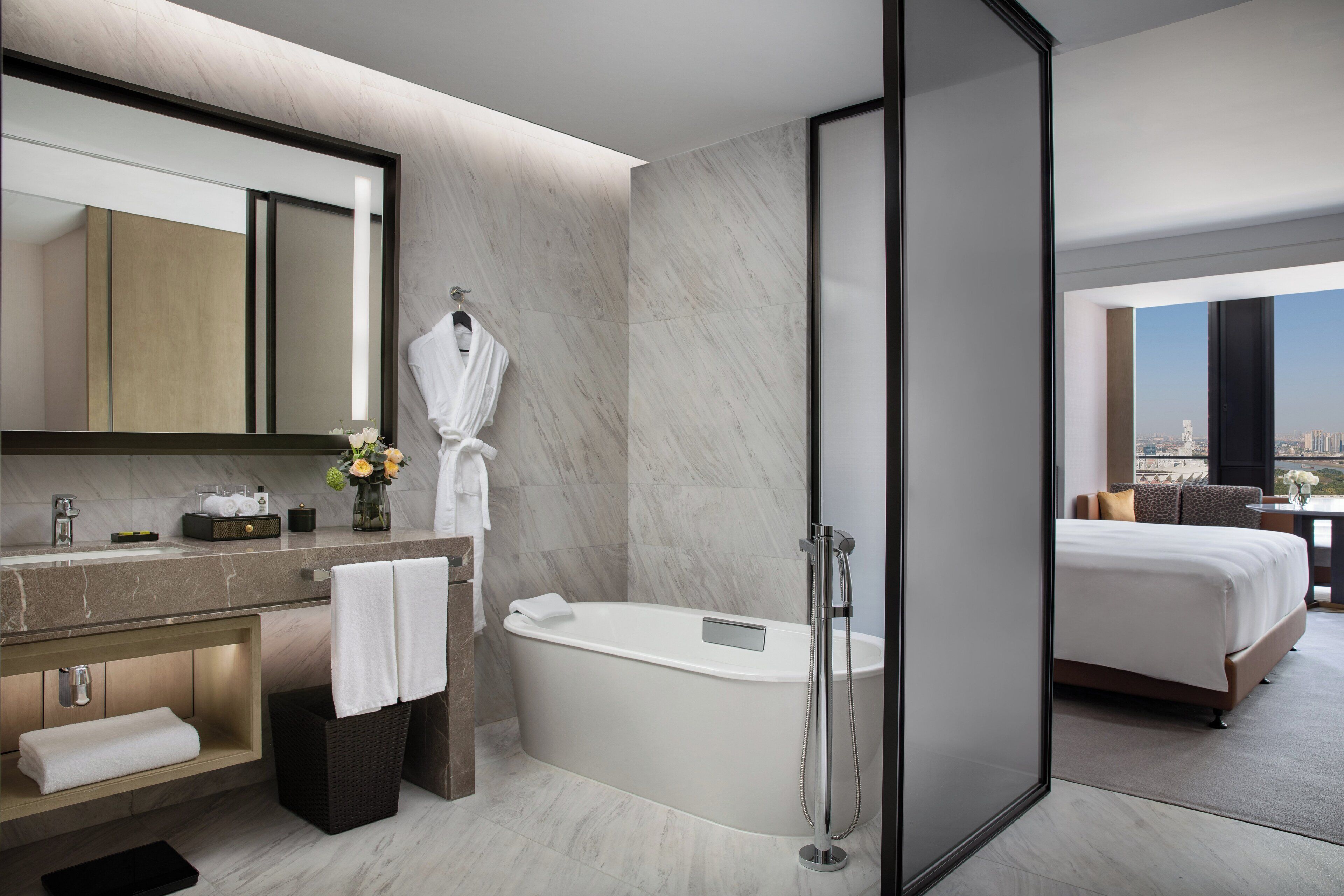 Ein modernes Hotelbad mit einer großen Badewanne, einem Waschtisch mit Spiegel und einer Duschkabine.