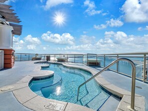 Un espace piscine offrant une vue dégagée sur l’océan, doté d’un parasol et d’un poste de surveillance pour les sauveteurs.