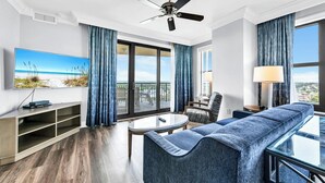 Ett modernt hotellrum med ett stort fönster, en takfläkt, en platt-TV, en soffa, ett soffbord och en lampa.