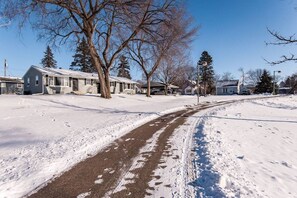 Une rue résidentielle bordée de maisons des deux côtés, une route enneigée et des arbres sans feuilles.