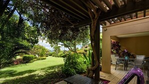 Un patio con una mesa y sillas de madera, un banco y vistas a un jardín y césped bien cuidados.
