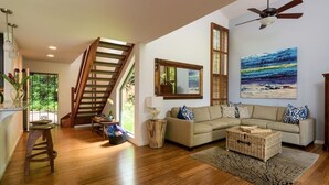 Un amplio salón con una escalera de madera, un cuadro grande y una zona de estar acogedora.