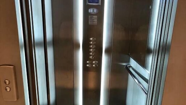 Een lift met een digitaal display, een metalen interieur en een glazen deur.
