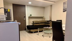 Een compacte leefruimte met een kitchenette, een bank, een glazen salontafel en een eethoek.