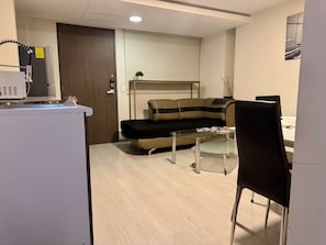 Un espacio habitable compacto con kitchenette, un sofá, una mesita de vidrio y un comedor.