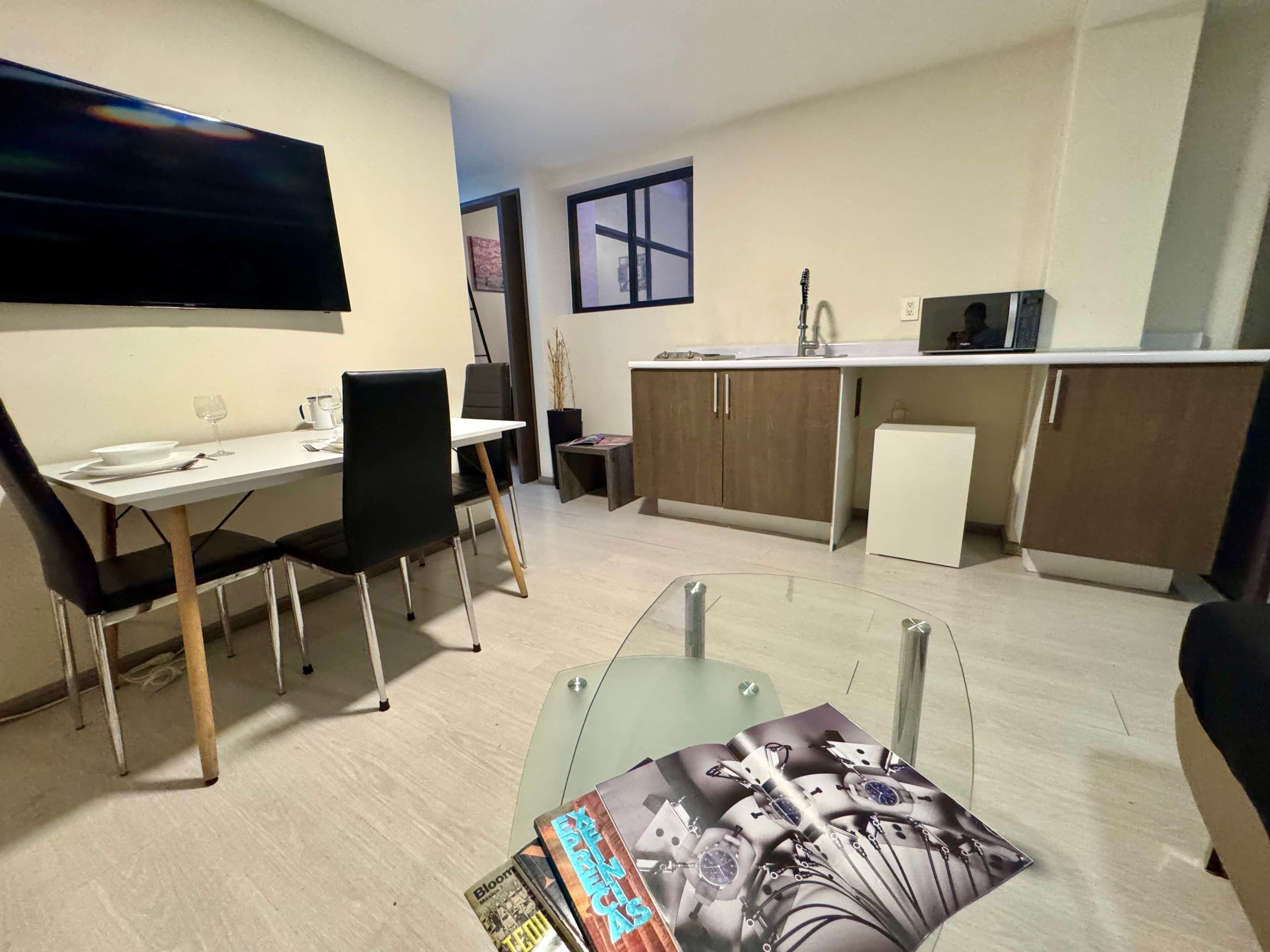 Un espacio habitable compacto con comedor, kitchenette y televisor de pantalla plana montado en la pared.