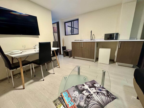 A compact living space with a dining area, kitchenette, and a flat-screen TV mounted on the wall.