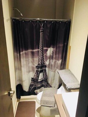 Une salle de bain avec un rideau de douche orné d’une représentation de la Tour Eiffel, des toilettes et un petit lavabo.
