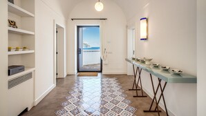 Un couloir moderne avec un sol carrelé, une porte en verre donnant sur un balcon et une longue table sur laquelle sont posés des bols.