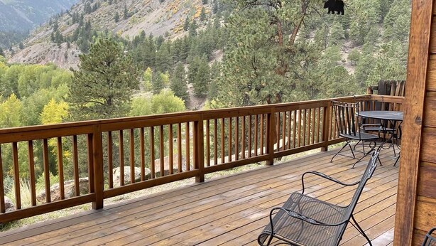 Eine Holzterrasse mit Metallstühlen, mit Blick auf eine gebirgige Landschaft.