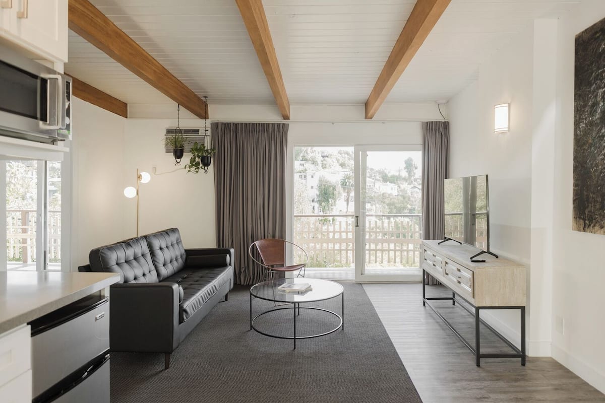 A modern living room with a sofa, a coffee table, a TV, and a kitchen area with a microwave.