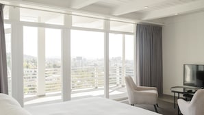 Quarto de hotel com uma cama grande, televisão, escrivaninha e vista para a cidade.