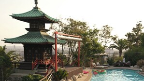 Área de piscina com espreguiçadeiras e uma estrutura em estilo pagoda ao fundo.