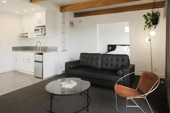 A modern living room with a sofa, a coffee table, and a chair. There is a kitchen area with white cabinets and a microwave. - Hollywood Hills Hotel (Los Angeles)