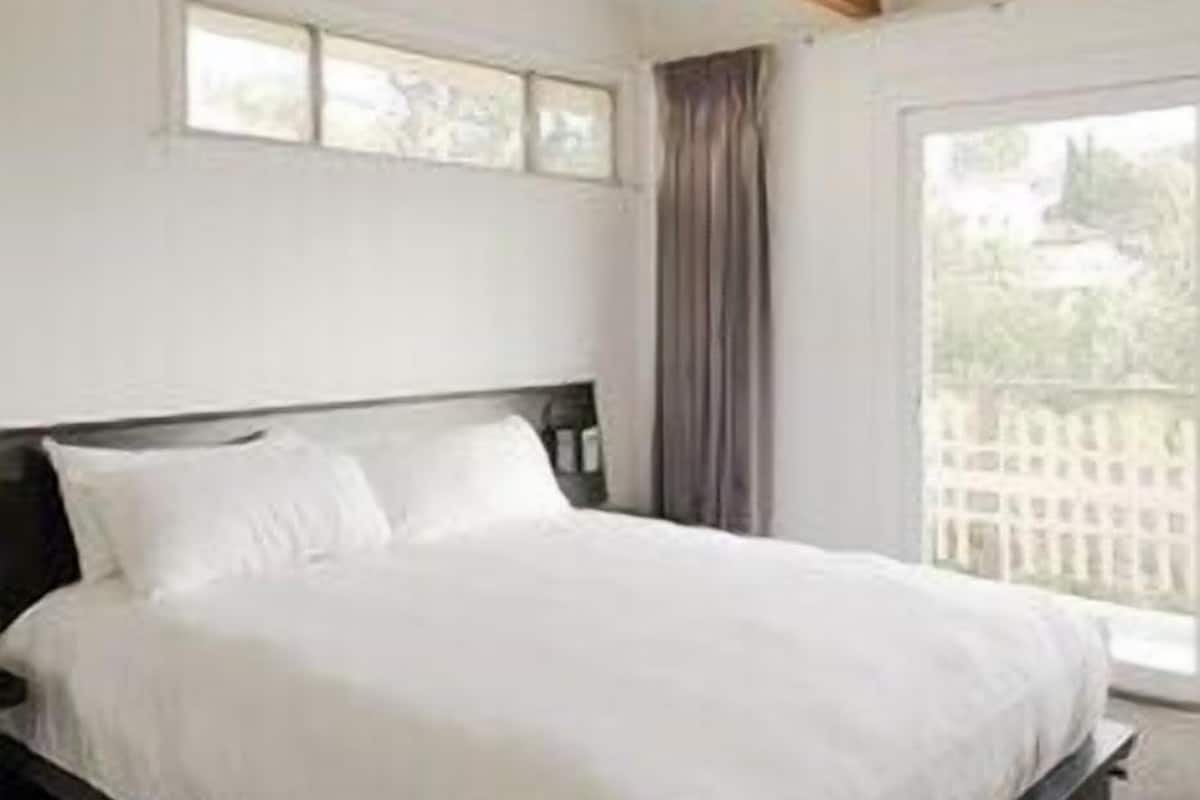 A bedroom with a bed, wooden ceiling beams, a window, and a view of greenery outside.