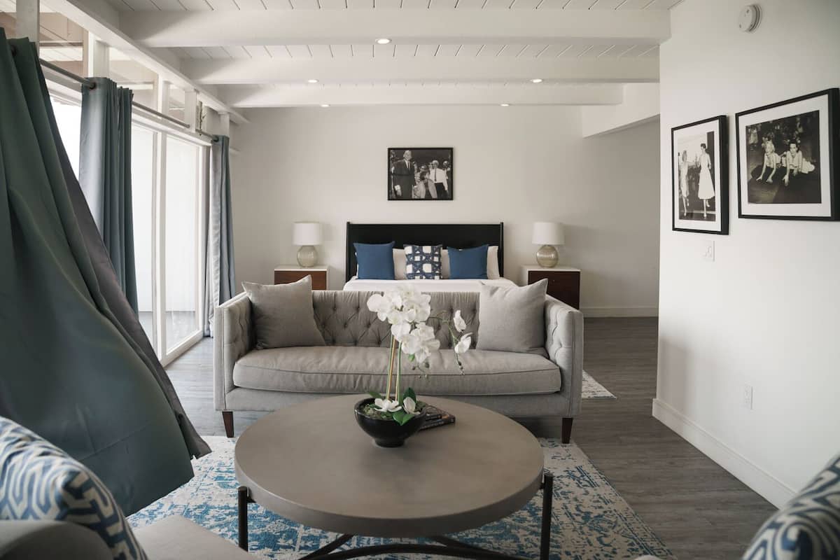 A modern hotel room with a large bed, a sofa, a coffee table, and a view of the outdoors.