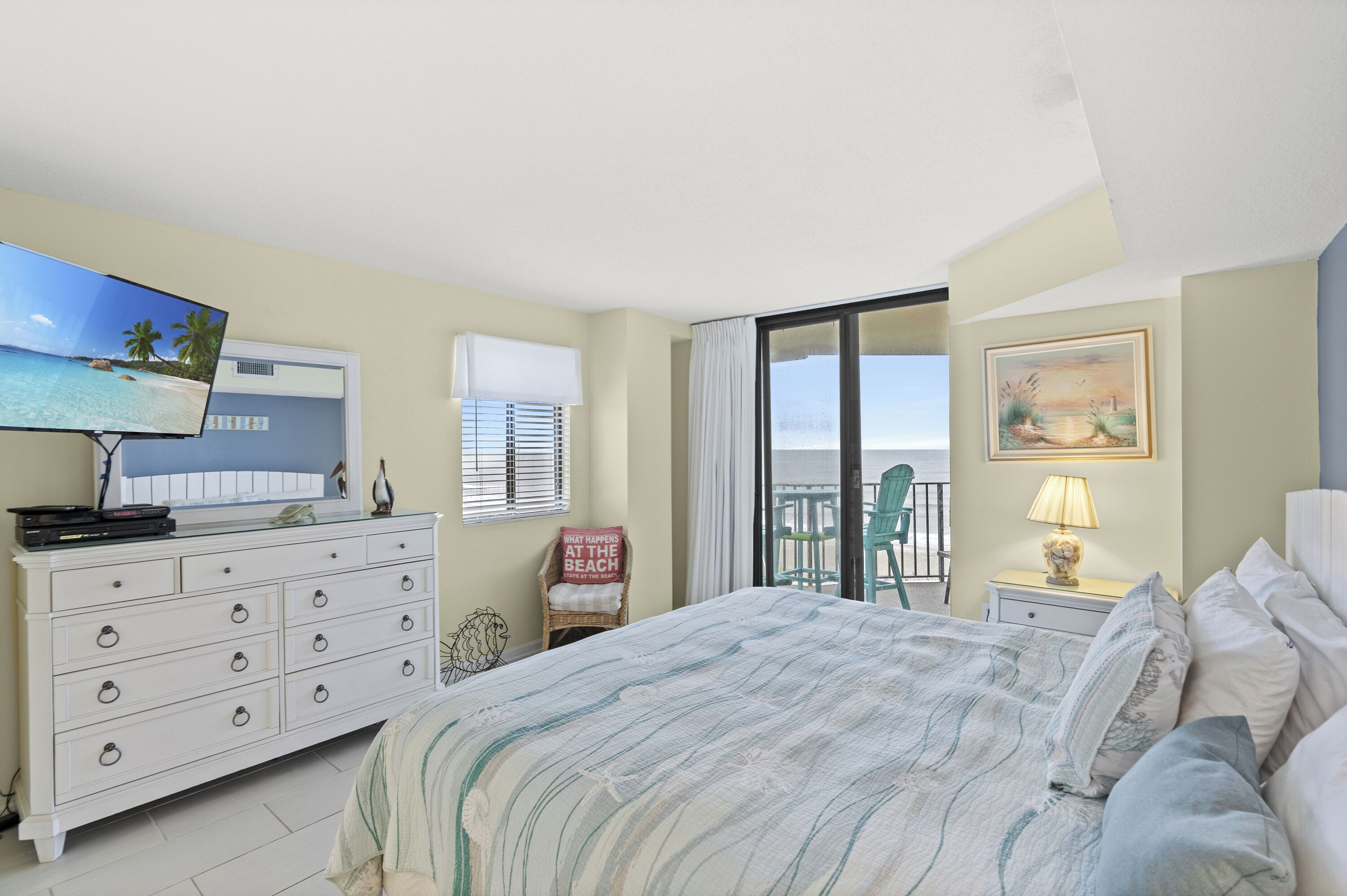 A bedroom with a bed, a dresser, a television, a window with blinds, a chair, and a painting.
