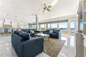 A spacious living room with a large sofa set, a coffee table, and a view of the sea through large windows.