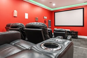 A home theater room with red walls, black leather seating, a large screen, and a projector.