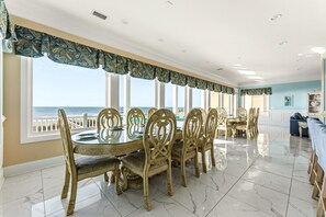 A dining area with a view of the ocean, featuring a round table with chairs, a chandelier, and a view of the sea through large windows.