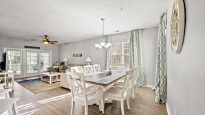 Un coin repas avec une table et des chaises blanches, un lustre et un ventilateur de plafond.