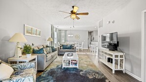 Un salon moderne avec un ventilateur de plafond, un canapé, une table basse et un téléviseur.
