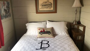 Een net opgemaakt bed met een gewatteerd patroon, een kussen met een auto-design en een ingelijst beeld aan de muur.