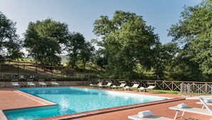 Una piscina rectangular con solárium de ladrillo, rodeada de sillones de descanso y una valla de madera.