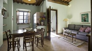 Un comedor con una mesa y sillas de madera, un refrigerador con flores, un sofá y una lámpara.