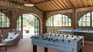 Una mesa de fútbol de mesa en una habitación con paredes de piedra, ventanas arqueadas y techo de madera.