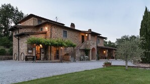 Un edificio de piedra con entrada de grava, mobiliario exterior y césped cuidado.