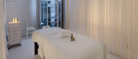 Habitación de hotel con cama, una silla, un armario pequeño y un baño con mampara de vidrio.
