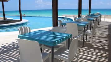 A beachside restaurant with outdoor seating overlooking a pool and the ocean.