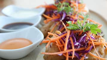 A plate with a piece of food topped with shredded carrots and purple cabbage, accompanied by two small bowls of sauce.