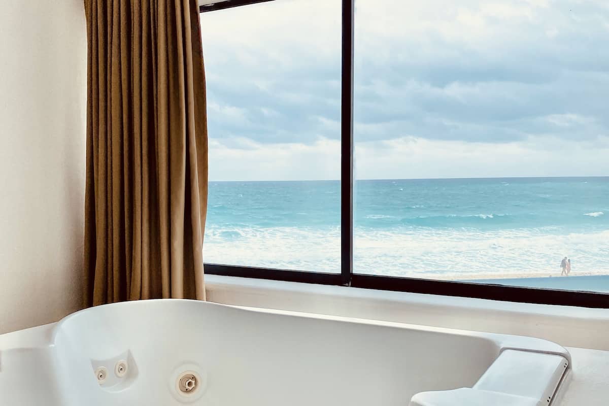 A modern bathroom with a large bathtub, a window with a view of the ocean, and a curtain.