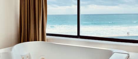Un baño moderno con una bañera grande, una ventana con vistas al océano y una cortina.