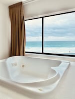 Uma casa de banho moderna com uma banheira grande, uma janela com vista para o oceano e uma cortina.