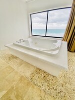 Un bagno moderno con una vasca freestanding, un'ampia finestra vista oceano e un pavimento strutturato.