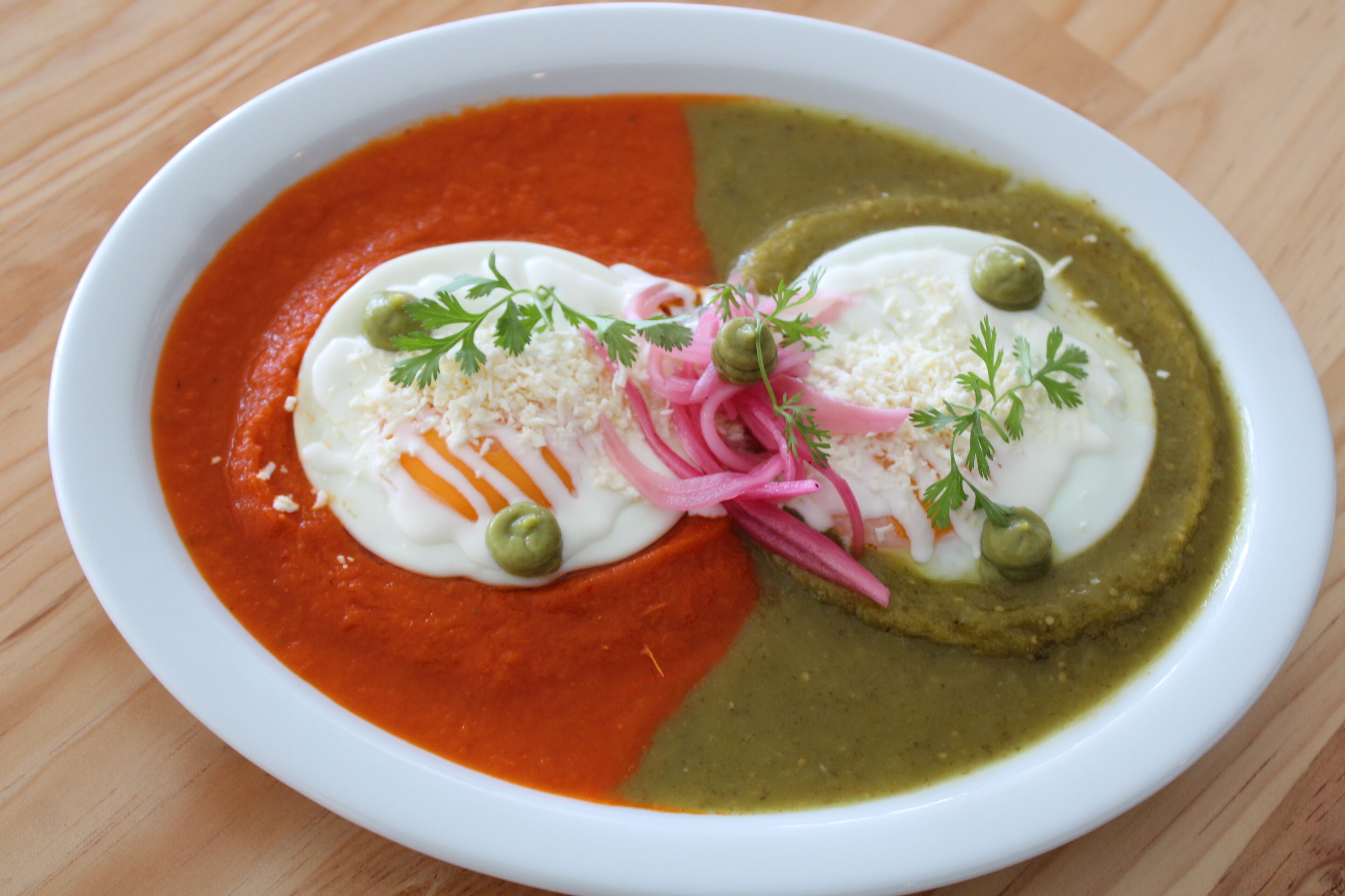 A white plate with two distinct sections of food, one red and one green, garnished with herbs and olives.