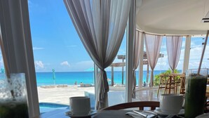 A dining table with a bowl of soup, a glass of green drink, and a cup of coffee. The table is set for two, with a view of the beach and ocean through large windows. - Cyan Cancun Resort & Spa  (Cancun)