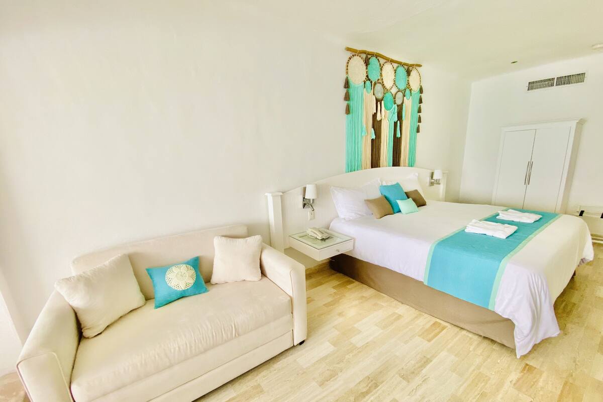 A hotel room with a bed, a sofa, a nightstand, and a wardrobe.