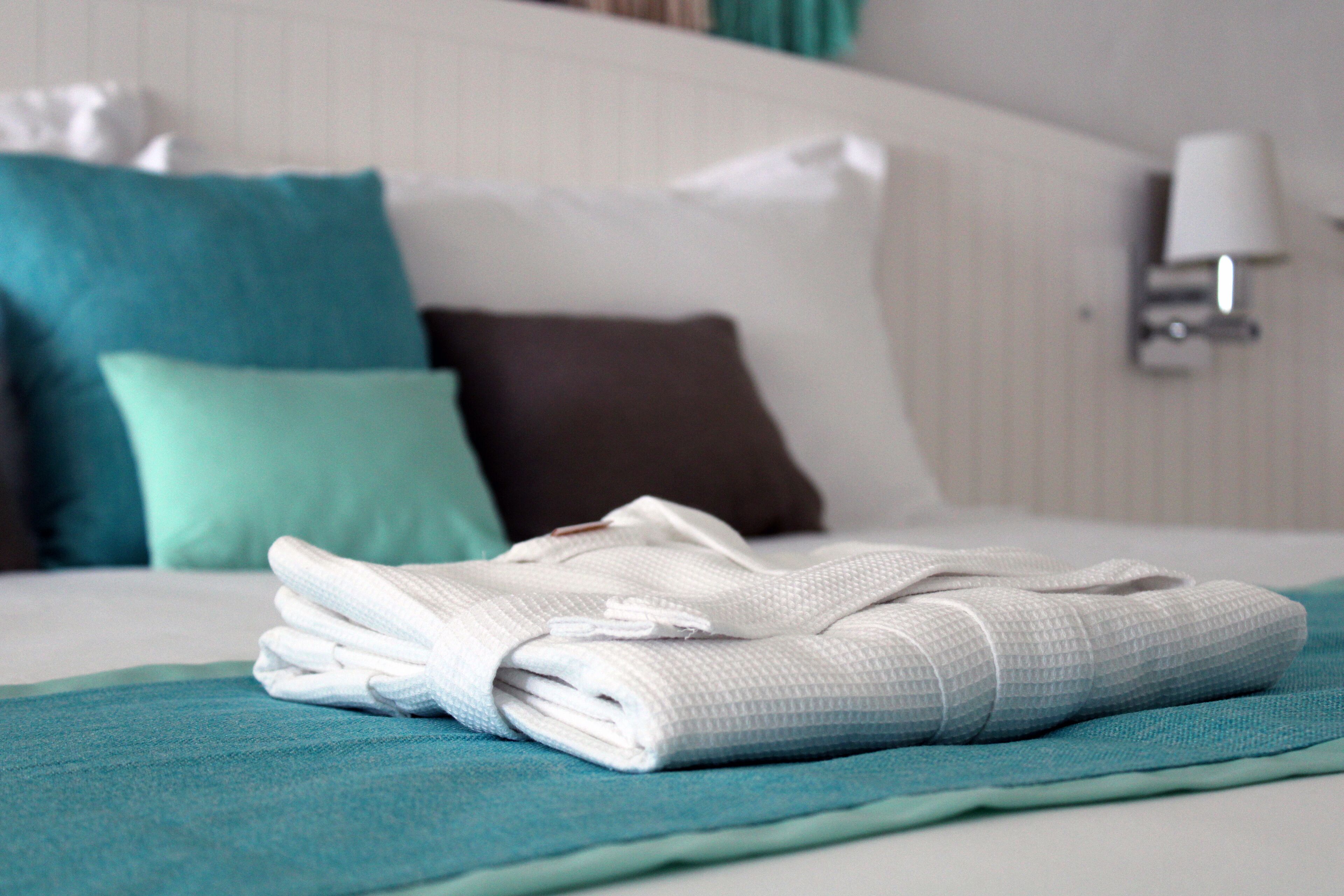 Un lit bien fait, avec une serviette blanche pliée et une couverture de couleur turquoise.