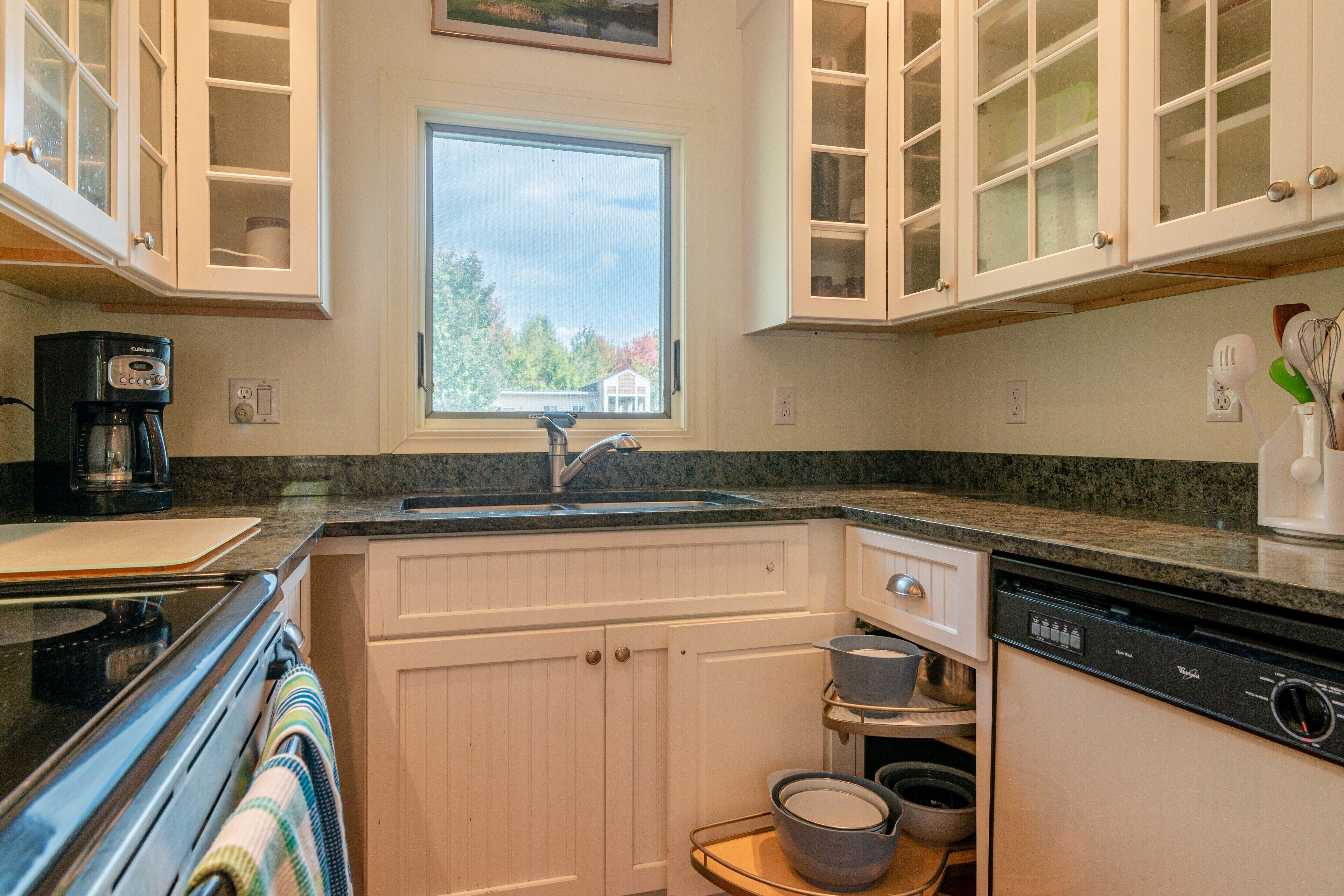 A kitchen with white cabinets, a window, a coffee maker, and a dishwasher.