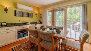 A dining area with a table set for four, surrounded by chairs, and a kitchen area with cabinets and a countertop. - Theatre in the Wood Too! - I’m the fancy sister (Stowe)