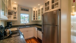 A modern kitchen with white cabinetry, a stainless steel refrigerator, and a granite countertop. - Theatre in the Wood Too! - I’m the fancy sister (Stowe)