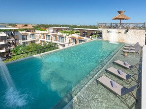 A rooftop infinity pool with clear blue water, lounge chairs, and a view of the surrounding buildings and landscape.