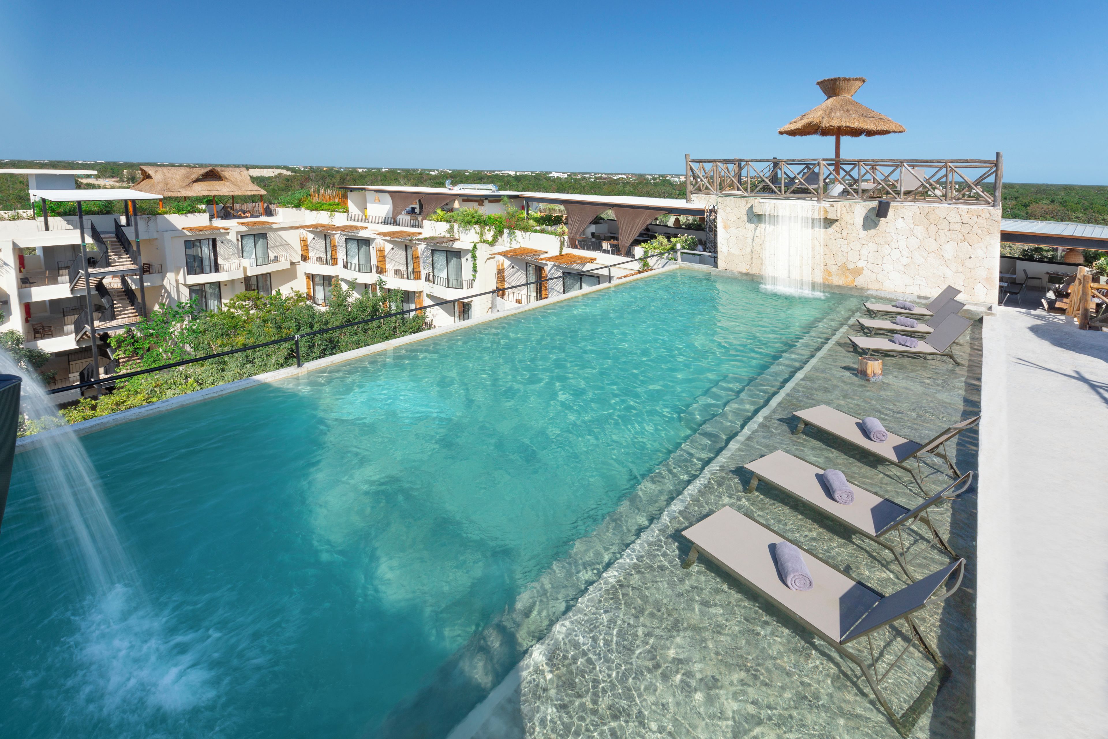 A rooftop infinity pool with clear blue water, surrounded by lounge chairs and a stone wall.